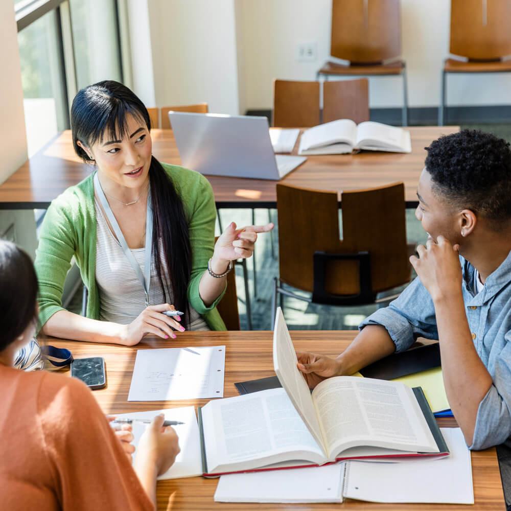 A group of people sitting around a table studying and discussing with open books and notebooks.