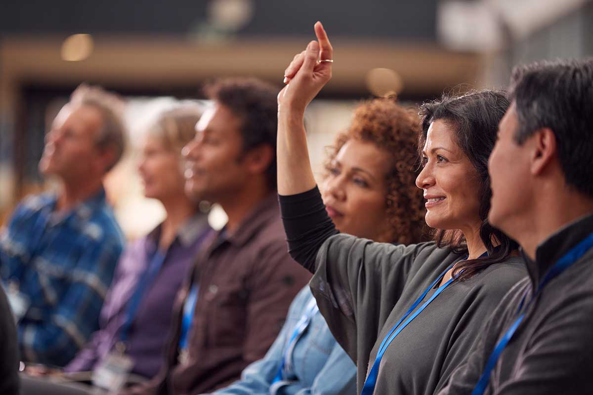 A group discussion where a woman raises her hand while others listen attentively.