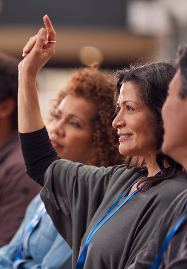A group discussion where a woman raises her hand while others listen attentively.